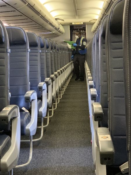 United staff applies a layer of electrostatic spray inside the cabin of an airplane to disinfect from germs.